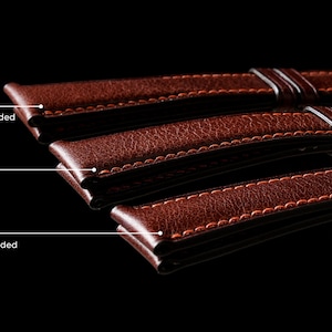 May include: Three brown leather watch straps with different padding styles: square padded, full padded, and domed padded. Each strap has orange stitching.