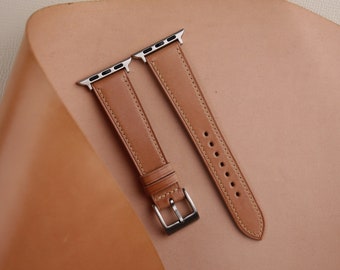May include: Two brown leather watch bands with silver clasps and stitching. The bands are laid out on a tan leather surface.