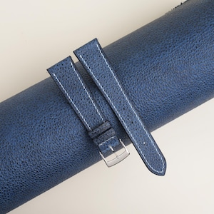 May include: Two blue leather watch straps with white stitching. The straps are rolled up and the buckle is visible.