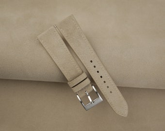 Könnte beinhalten: Zwei beigefarbene Armbänder aus Wildleder mit einer silbernen Schließe.