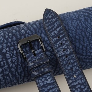May include: A blue leather watch strap with a black buckle. The strap has a textured, patterned surface.