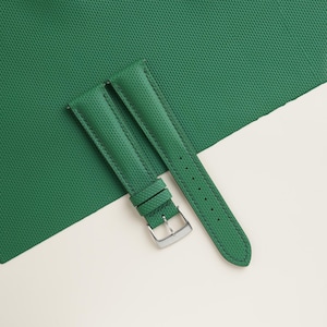 May include: A pair of green watch straps with a textured surface. The straps are made of a durable material and feature a silver-colored buckle. The straps are displayed on a white and green background.