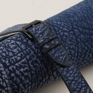 May include: A close-up of a dark blue leather watch strap with a black buckle. The strap has a textured, embossed pattern that resembles elephant skin.