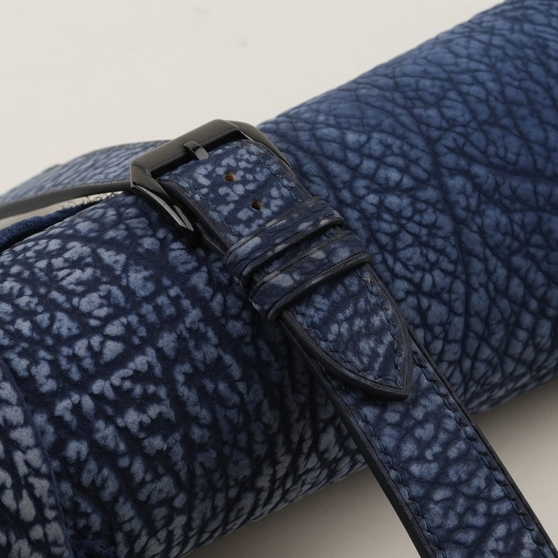 May include: A close-up of a dark blue leather watch strap with a black buckle. The strap has a textured, embossed pattern that resembles elephant skin.