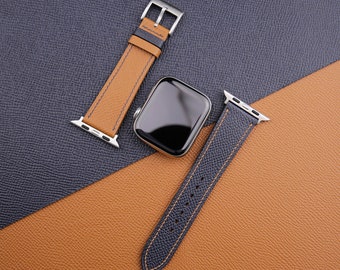 May include: Two watch bands, one brown with tan stitching and one blue with black stitching, are laid out on a brown and blue textured surface. A silver Apple Watch face is in the center of the image.