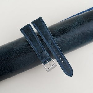 May include: A dark blue leather watch strap with white stitching and a silver buckle.