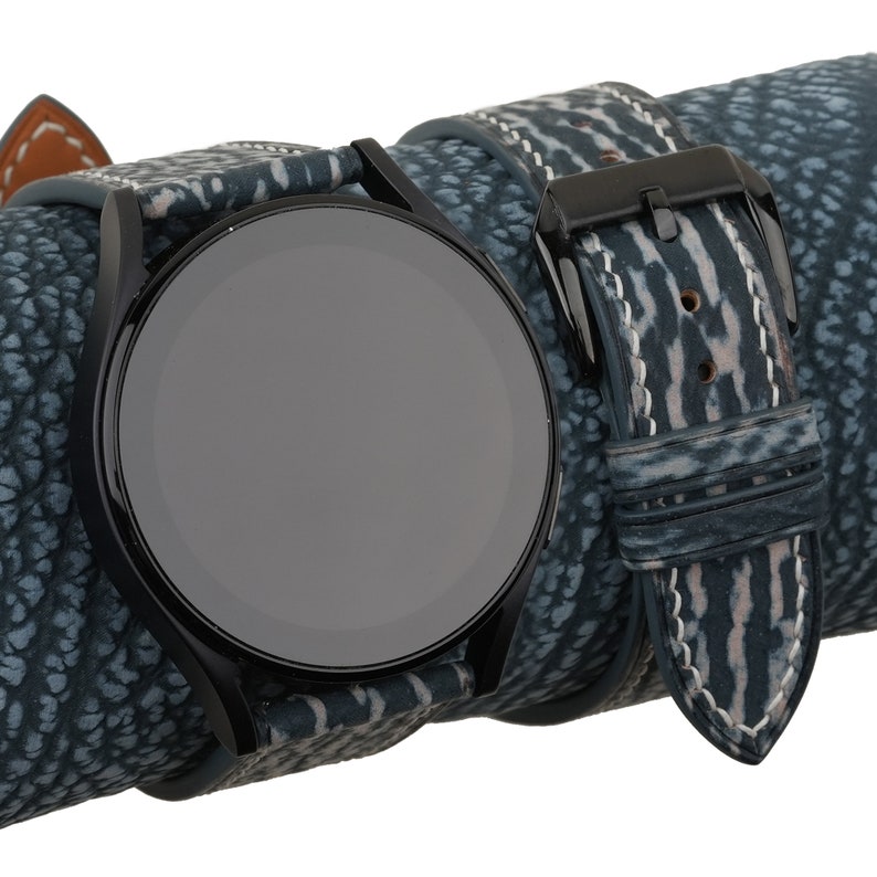May include: A black watch with a blue and white patterned leather band. The watch face is black and round.