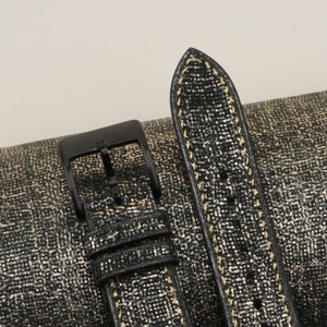 K&ouml;nnte beinhalten: Schwarzes Lederarmband mit goldenen N&auml;hten. Das Armband hat einen Schlie&szlig;enverschluss und ein strukturiertes Muster.