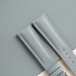 Puede incluir: Primer plano de dos correas de reloj gris claro con una superficie texturizada y costuras blancas. Las correas est&aacute;n hechas de un material duradero y tienen un dise&ntilde;o cl&aacute;sico. Las correas de reloj son de color neutro y se pueden combinar con varias esferas.