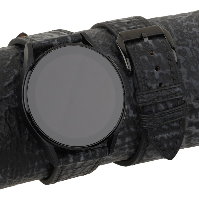 May include: A black smartwatch with a black leather band. The band has a textured pattern.
