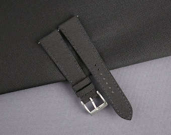 May include: A black watch strap with a silver buckle. The strap is made of a textured fabric.