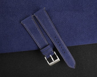 Könnte beinhalten: Zwei blaue Wildleder-Uhrenarmbänder mit einer silbernen Schließe. Die Armbänder liegen auf einer blauen Wildlederfläche.