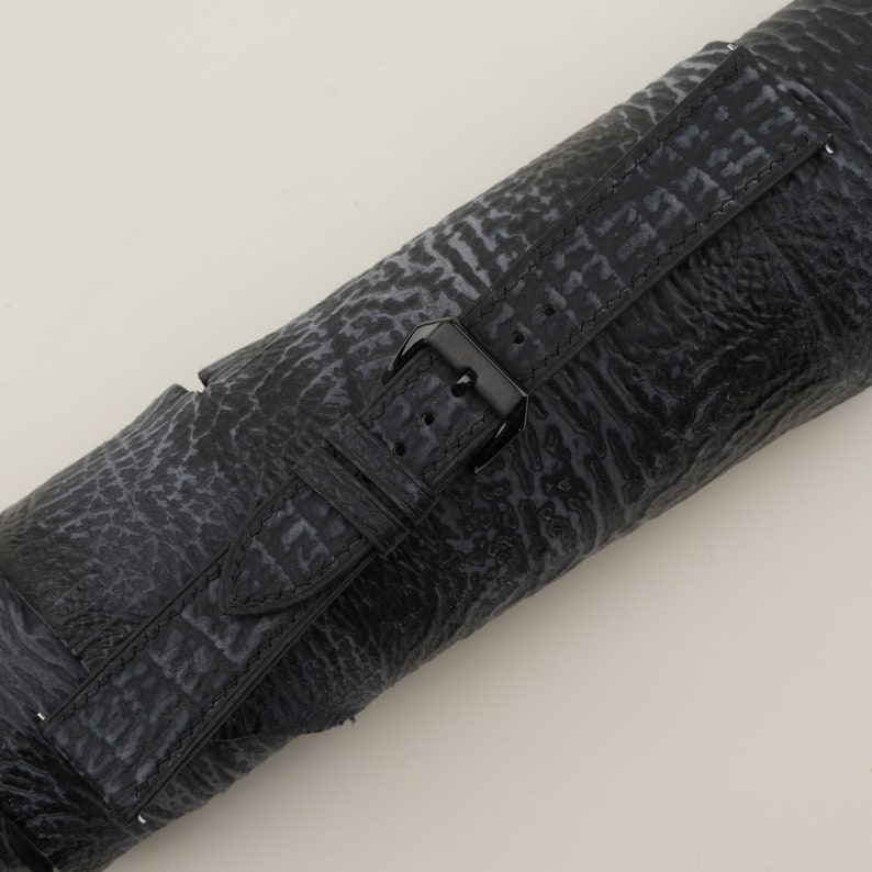 May include: Black leather watch strap with a black buckle. The strap has a textured pattern.