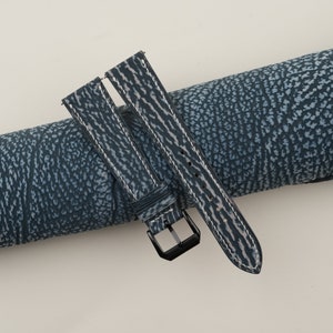 May include: A blue leather watch strap with white stitching and a black buckle.