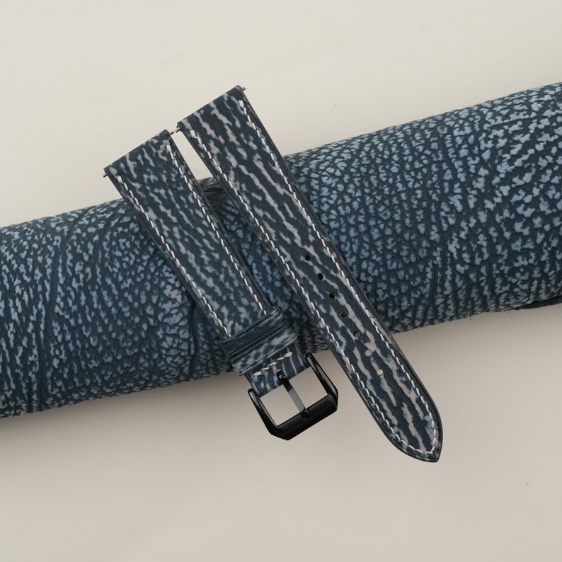 May include: A blue leather watch strap with white stitching and a black buckle.