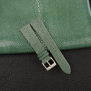 May include: A green leather watch strap with a silver buckle. The strap is made of stingray skin and has a textured surface.