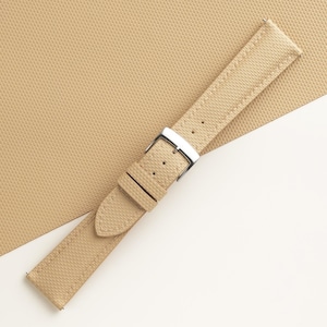 Puede incluir: Correa de reloj de color beige con superficie texturizada y hebilla plateada. La correa tiene un dise&ntilde;o cl&aacute;sico con m&uacute;ltiples orificios de ajuste. La correa del reloj est&aacute; hecha de un material duradero y es adecuada para varios estilos de reloj.