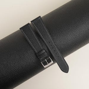 May include: Two black leather watch straps with a silver buckle. The straps are rolled up and have a textured surface.