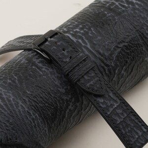May include: Black leather watch strap with a black buckle. The strap has a textured surface and is rolled up.