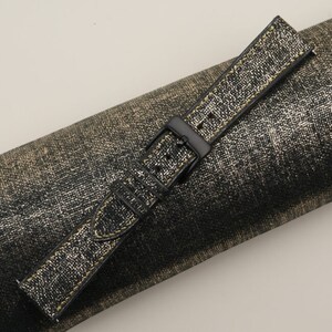 K&ouml;nnte beinhalten: Ein schwarzes Lederarmband mit goldenen N&auml;hten. Das Armband liegt auf einer gold-schwarzen, strukturierten Oberfl&auml;che.