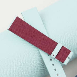May include: A light blue and burgundy leather watch strap with a textured finish.