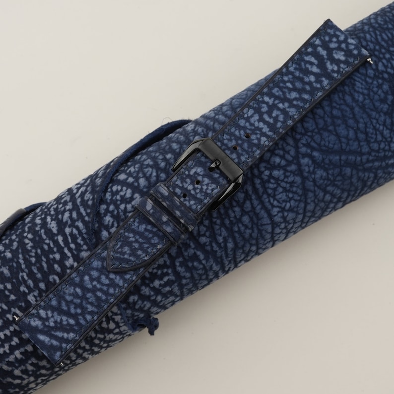 May include: A blue leather watch strap with a black buckle. The strap has a textured pattern that resembles elephant skin.