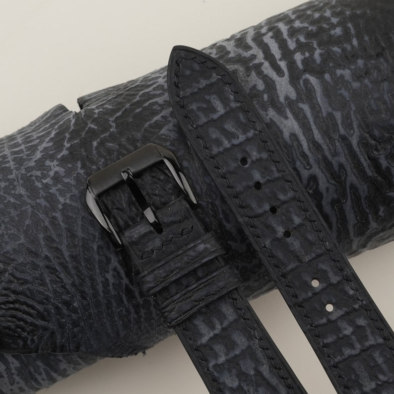 May include: Black leather watch strap with a black buckle. The strap has a textured, alligator-like pattern.