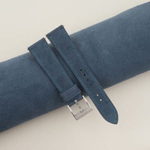 May include: Two blue suede watch straps with a silver buckle. The straps are laid out on a blue suede surface.