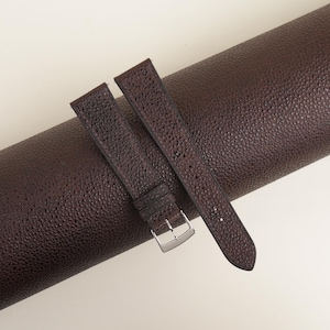 May include: Two brown leather watch straps with a textured finish. The straps are rolled up and have a silver buckle.