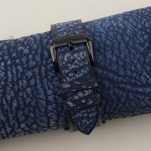 May include: A blue leather watch strap with a black buckle. The strap has a textured surface and is rolled up.