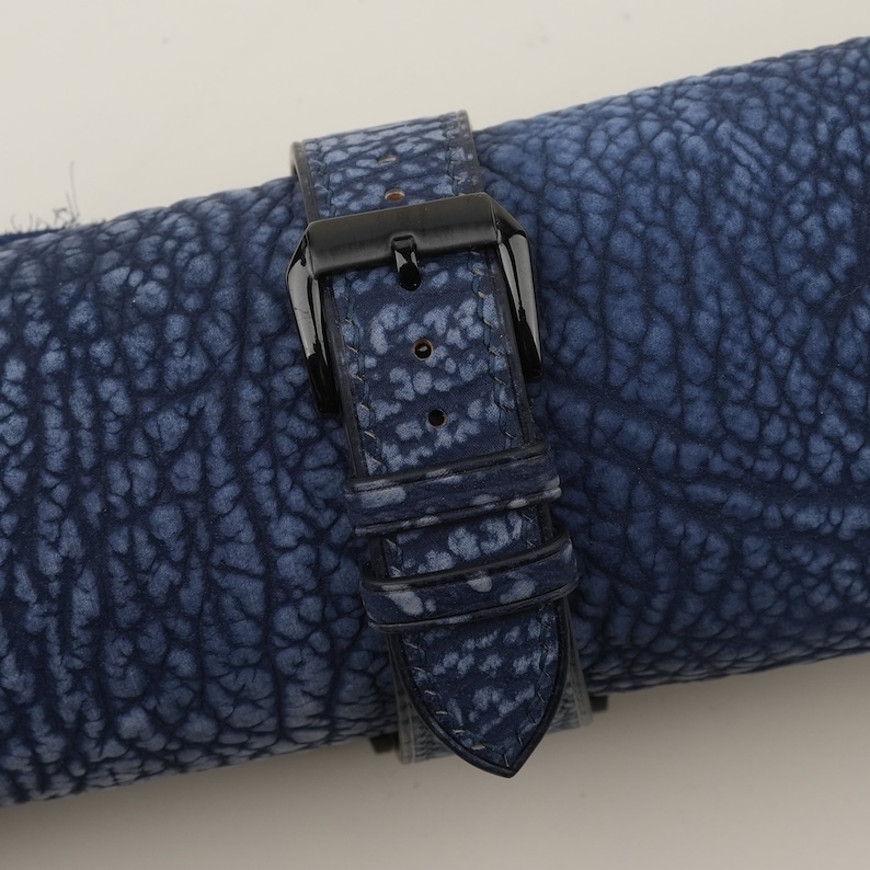 May include: A blue leather watch strap with a black buckle. The strap has a textured surface and is rolled up.