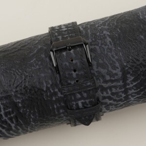 May include: Black leather watch strap with a black buckle. The strap has a textured pattern.