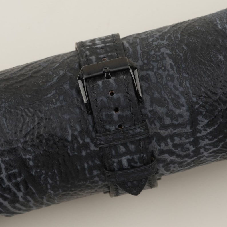 May include: Black leather watch strap with a black buckle. The strap has a textured pattern.