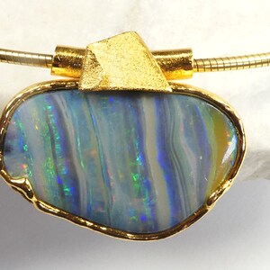 Könnte beinhalten: Eine goldene Halskette mit einem großen Opal-Anhänger. Der Opal ist blau-grün mit schillernden Farbeffekten. Der Anhänger ist in einer goldenen Fassung gefasst.