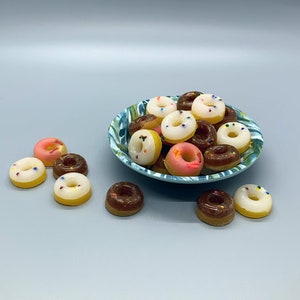 May include: A blue and green patterned bowl filled with mini donuts in various colors, including pink, white, and brown.  There are also a few donuts on a white surface next to the bowl.