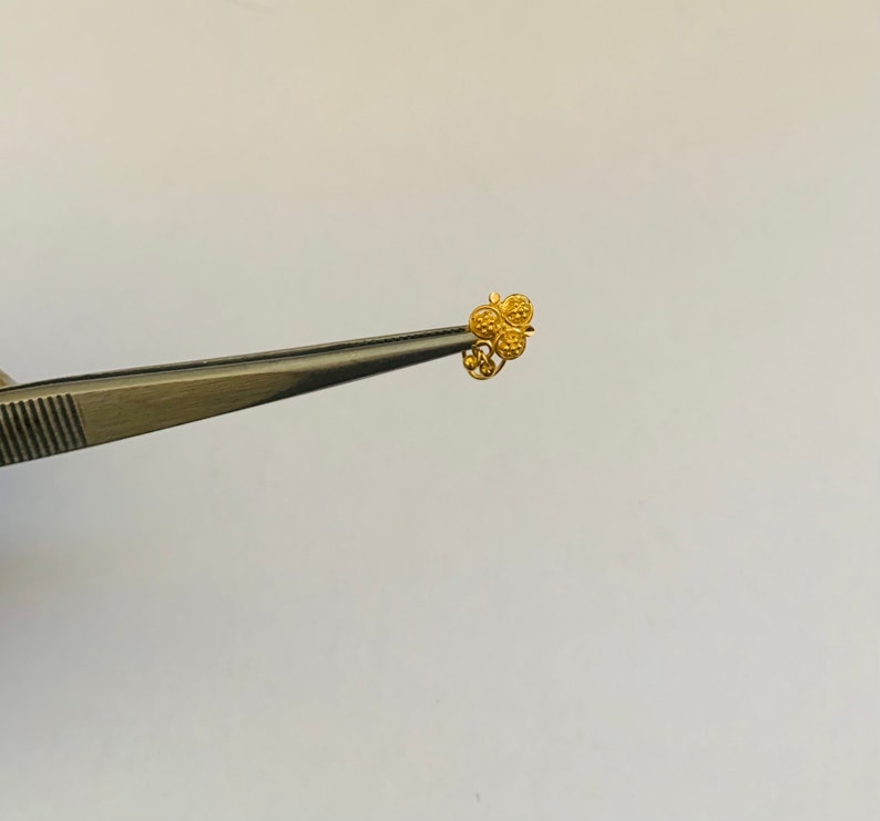 May include: A gold nose ring with a three-leaf clover design.