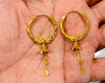 May include: A pair of gold hoop earrings with a dangling charm. The charms are shaped like bells and have a chain attached to them.