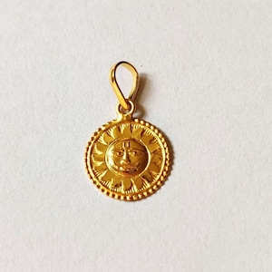 May include: A gold pendant featuring a sun with a face and a symbol on its forehead. The pendant is round and has a detailed design.