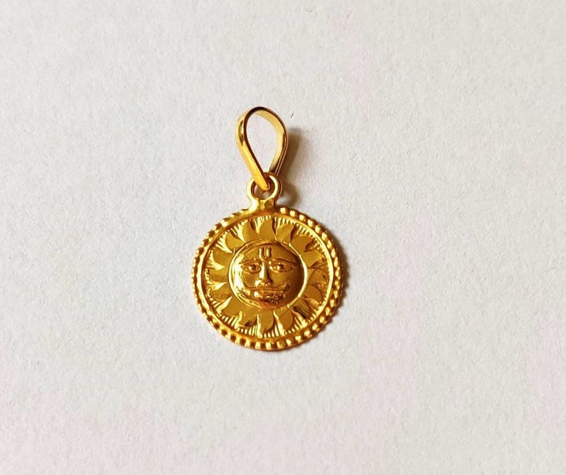 May include: A gold pendant featuring a sun with a face and a symbol on its forehead. The pendant is round and has a detailed design.