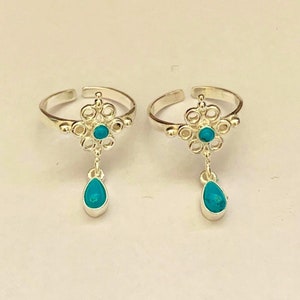 Op de afbeelding: Een paar zilveren teenringen met turquoise stenen. Elke ring heeft een hangende turquoise traan.