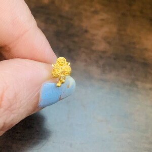 May include: A gold nose ring with a clover design. The clover has four leaves, each with a textured surface.