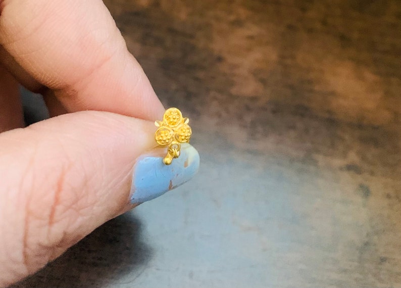 May include: A gold nose ring with a clover design. The clover has four leaves, each with a textured surface.