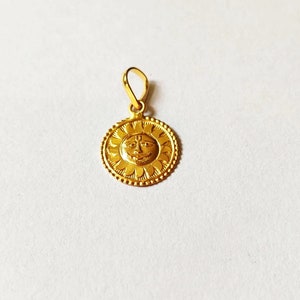 May include: A gold pendant featuring a sun with a face in the center. The sun is surrounded by a circle of small flowers.