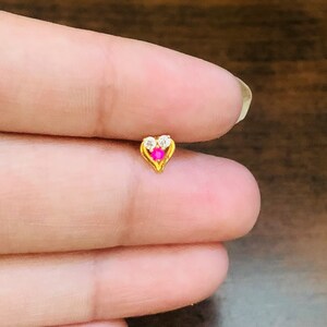 May include: A gold heart-shaped nose ring with a pink gemstone and two clear gemstones.