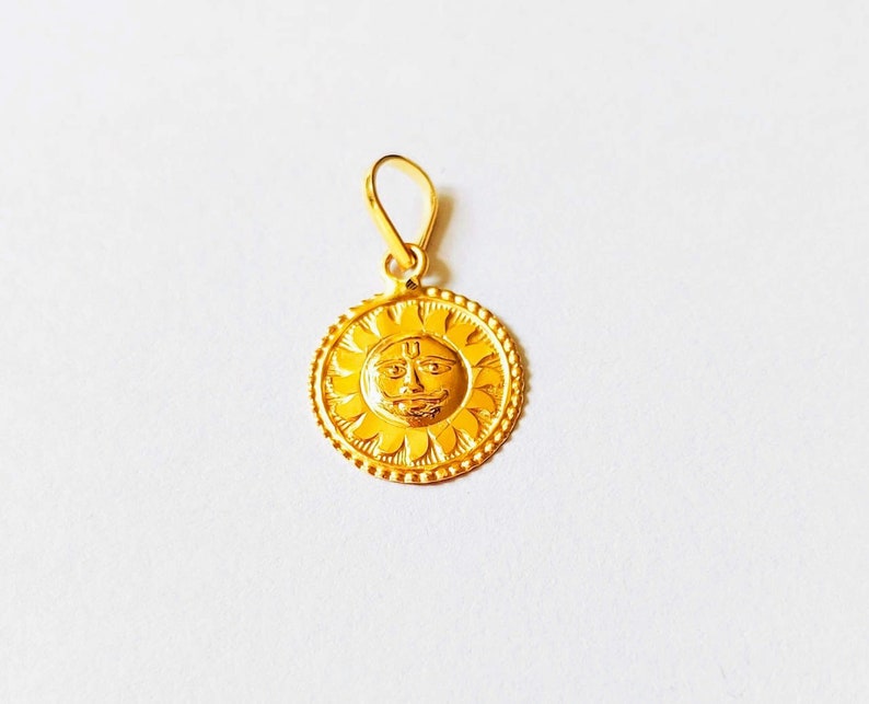 May include: A gold pendant featuring a sun with a face and a "U" symbol in the center. The pendant is on a white background.