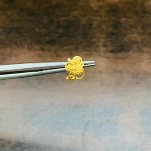 May include: A gold nose ring with a flower design. The flower has five petals, each with a textured surface.