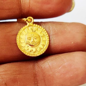 May include: Gold pendant featuring a sun with a face and a symbol on the forehead. The pendant is surrounded by a circular design.