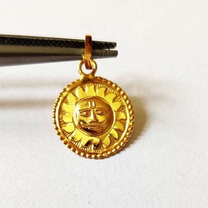 May include: A gold pendant featuring a sun with a face, surrounded by a floral design. The pendant has a loop at the top for attaching to a chain.