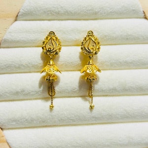 Könnte beinhalten: Ein Paar goldene Ohrringe mit einem tropfenförmigen Design und einem kleinen Glockenanhänger. Die Ohrringe haben eine zarte Kette, die von der Glocke hängt.