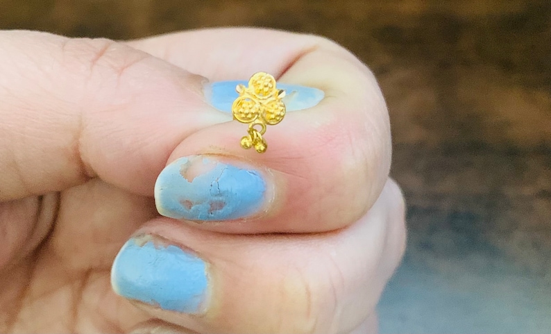 May include: A gold nose ring with a floral design. The ring has three round flowers with a small dangling charm.